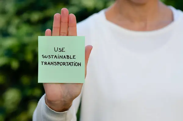 Elinde yeşil el yazısı olan bir kadın sürdürülebilir ulaşımı hatırlatan bir tabela tutuyor..