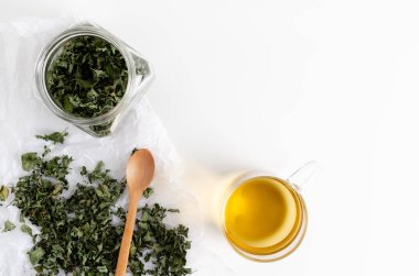 Bir fincan nane çayı ve bir kavanozda kurutulmuş nane yaprağı ve beyaz arka planda beyaz bir kağıt üzerinde. Üst görünüm.