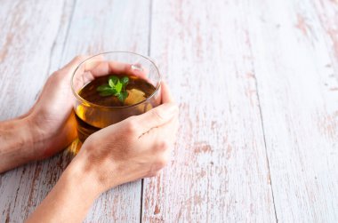 Hafif ahşap arka planda fotokopi alanı olan bir fincan bitki çayı tutan kadın eller..