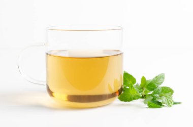 Şeffaf bir fincan nane çayı ve beyaz arka planda taze nane yaprakları. Ön görünüm.