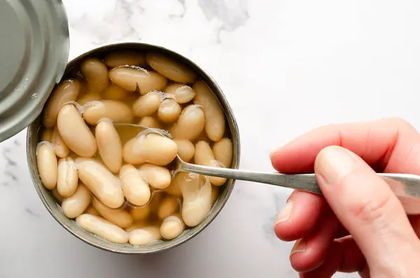 Beyaz fasulye konservesinde kaşıkla elini kapat. Üst görünüm ve boşluk kopyala. Gıda koruma kavramı.