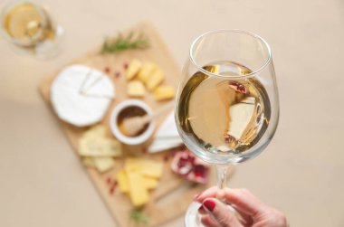 Bir kadın eli bir bardak beyaz şarap ve bir kadeh daha beyaz şarap ve sırtı peynirli ahşap tahta ve nar tohumlarıyla dolu.. 