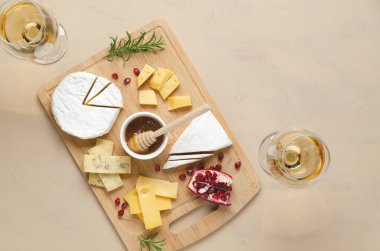 İki bardak beyaz şarap ve çeşitli peynir, bal, nar tohumu ve biberiye yaprakları ahşap bir tahtanın üzerinde ve fotokopi alanı olan bej arka plan. Üst görünüm ve yatay biçim.