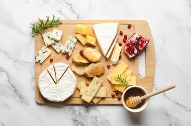 Mermer zemin üzerinde, üzerinde kopya alanı olan ahşap bir tahtanın üzerinde çeşitli peynir ve nar tohumları. Üst görünüm ve yatay biçim.