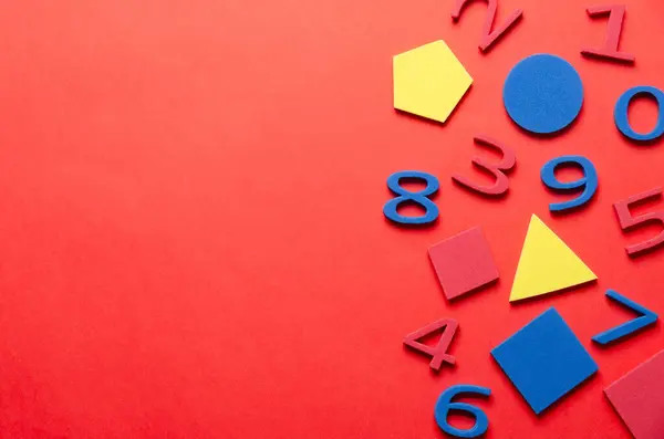 Kırmızı arka planda renkli köpük numaraları ve geometrik şekiller ve kopyalama uzayı. Okul konseptine dönelim.. 
