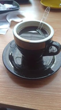 Dumanı tüten siyah bir Americano kahvesi, zengin ve koyu, basit bir fincanda servis ediliyor, ferahlatıcı ve aromatik bir kahve deneyimi için mükemmel..