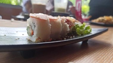 Taze malzemelerle lezzetli bir suşi rulosu, aroma ve dokuların mükemmel dengesi, yosunla sarılmış ve sosla servis edilmiş.