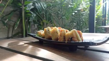 Taze malzemelerle lezzetli bir suşi rulosu, aroma ve dokuların mükemmel dengesi, yosunla sarılmış ve sosla servis edilmiş.