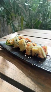 Taze malzemelerle lezzetli bir suşi rulosu, aroma ve dokuların mükemmel dengesi, yosunla sarılmış ve sosla servis edilmiş.