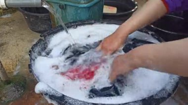 Eller sabunlu su dolu bir havuzda giysileri ovalıyor, geleneksel el yıkama yöntemlerini, günlük ev işlerini ve basit ev yaşamını yakalıyor..