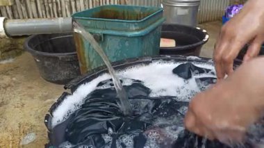 Eller sabunlu su dolu bir havuzda giysileri ovalıyor, geleneksel el yıkama yöntemlerini, günlük ev işlerini ve basit ev yaşamını yakalıyor..