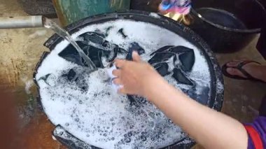 Eller sabunlu su dolu bir havuzda giysileri ovalıyor, geleneksel el yıkama yöntemlerini, günlük ev işlerini ve basit ev yaşamını yakalıyor..