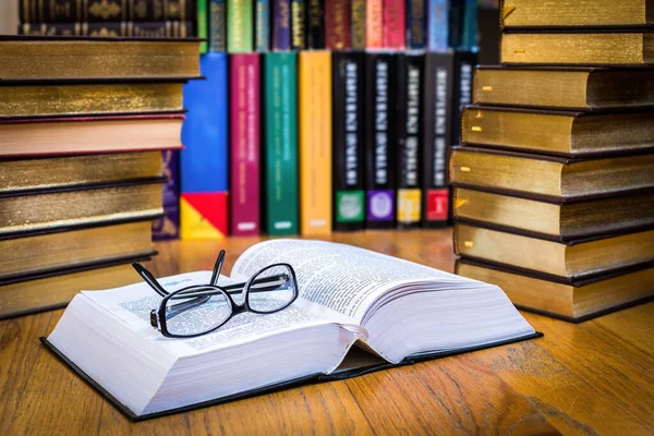 Stock image Selected focus close-up of an open book with reading eyeglasses, on a library desk.