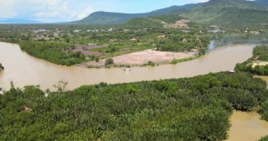 aerial drone shot of a small boat sailing up a river surrounded by green nature. Mountains as backdrop  