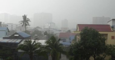 Şiddetli yağmur, evlerin üzerinden esen rüzgarlar. Arka planda Sihanoukville binaları 