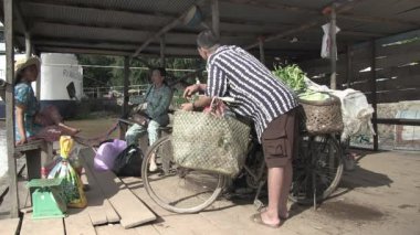 Kampong Cham - Kamboçya - 10-21-2013; bisikletli sebze satıcısı ve feribot sepetli ve çantalı kadınlar arka planda demirlemiş bir yolcu gemisinden bahsediyorlar.