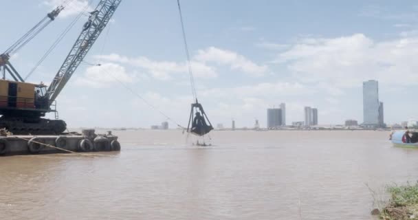 バージに取り付けられたバケツの浚渫船は 川の一部から堆積物を除去し 川の別の部分に戻しました プノンペン首都を背景に — ストック動画
