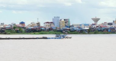 Kum mavnası nehirde yelken açarken balıkçı teknesi geçiyor. Arka plan olarak Asya köyü