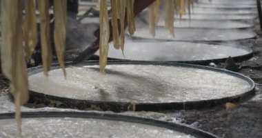 Sıcak soya sütü soğudukça, yüzeyinde ince bir katman oluşur. Bir işçi bıçağı ikiye bölmek için kullanır ve ince çarşafları bambu şeridine asar..