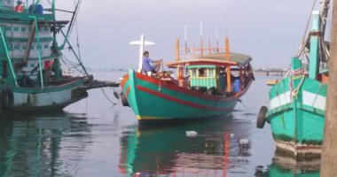 Sihanoukville, Kamboçya - 06.09.2023; balıkçı teknesinin pruvasında oturan bir balıkçı balıkçı limandan ayrılıyor
