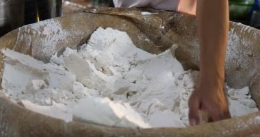 Bir işçinin pirinç hamurundan bir parça alıp yoğurmak için makineye koyduğu yakın plan.