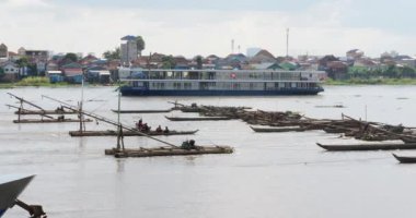 Bambu balıkçı tekneleri, ağları önde asılı, sakin varlıkları arka planda yüzen görkemli nehir yolcu gemisiyle çelişiyor..