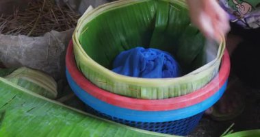 Plastik sepeti muz yapraklarıyla sarmayı bitiren bir kadının yakın çekimi. Bu sepette pirinç eriştesi kullanılacak..
