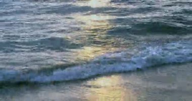 Güneşin batışının yansımasıyla kumlu bir sahile vuran dalgalara yaklaş