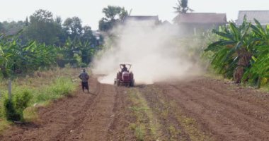 Toprağı ekime hazırlamak için traktör kullanan bir çiftçinin ön görüntüsü tozlu bir ortam yaratıyor..