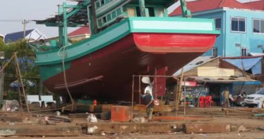 Sihanoukville - Kamboçya - 03.17.2024; Yeni restore edilmiş ahşap bir balıkçı teknesinin arka görüntüsü sola kayıkhaneye doğru hareket ediyor.