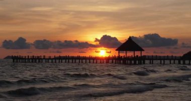 Balkonu olan ahşap iskele bulutlu bir günbatımında dalgalarla okyanusa doğru uzanıyor..