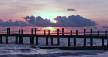 Yıpranmış ahşap iskele dalgalara doğru çıkıyor. Bulutlu bir günbatımı gökyüzünü alevli renklerle tutuşturur..