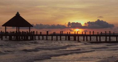 Ahşap bir iskelede, bir çardakla okyanusa doğru uzanır bulutlu bir günbatımında dalgalarla..