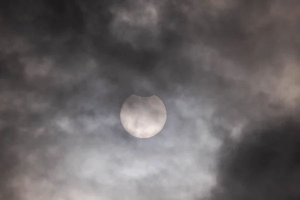 Solar eclipse on a cloudy day. Cloudy sky, the sun can be seen from behind a thin layer of clouds during a partial eclipse. The upper part of the sun is obscured by the moon. There are spots in the sun.