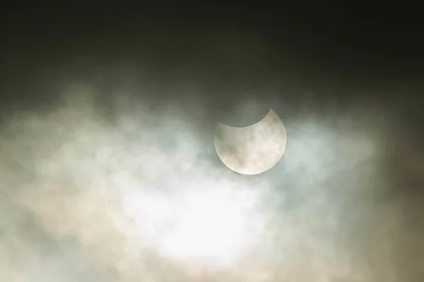 Solar eclipse on a cloudy day. Cloudy sky, the sun can be seen from behind a thin layer of clouds during a partial eclipse. The upper part of the sun is obscured by the moon. There are spots in the sun.