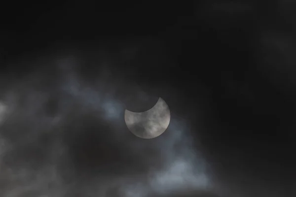 Solar eclipse on a cloudy day. Cloudy sky, the sun can be seen from behind a thin layer of clouds during a partial eclipse. The upper part of the sun is obscured by the moon. There are spots in the sun.