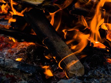 Küçük bir yığın halinde kesilmiş odun parçaları. Üzerlerinde yanan şenlik ateşinin alevleri uçuşuyor. Ahşap siyahtır ve bir kül tabakasıyla kaplıdır..