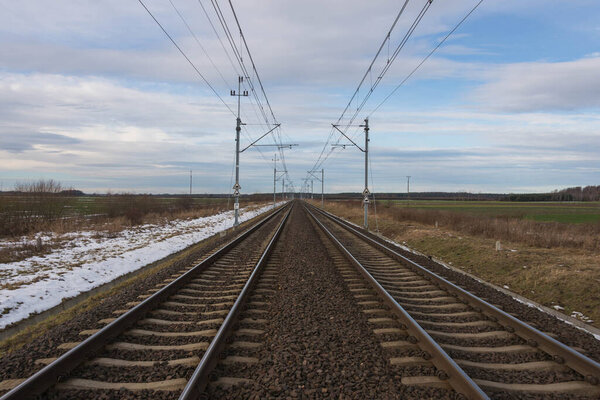 Double-track railway. There are bushes and trees on both sides. A thin layer of white snow covers the ground and trees.