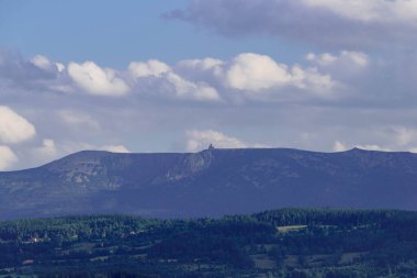 Yukarısı kozalaklı ormanlarla kaplı. Yuvarlanan arazi. Uzakta dağların zirvelerini görebilirsiniz. Hassas bir sis tarafından gizlenmiş. Gökyüzü biraz bulutlu..