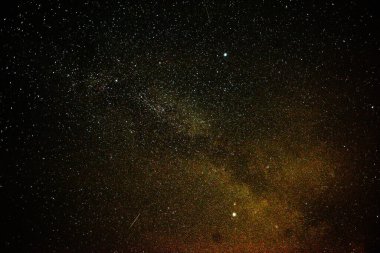 Geceleri bulutsuz gökyüzü. Gökyüzü sayısız yıldızla kaplı ve çerçevenin ortasında parlayan bir nebula görebilirsiniz..