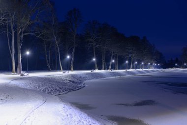 Gece vakti, kış manzarasında bir gölet. Göletin yüzeyi buzla kaplıdır, kıyı beyaz kar tabakasıyla kaplıdır. Gölün etrafında bir patika var. Banklar ve fenerler var..