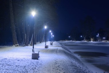 Gece vakti, kış manzarasında bir gölet. Göletin yüzeyi buzla kaplıdır, kıyı beyaz kar tabakasıyla kaplıdır. Gölün etrafında bir patika var. Banklar ve fenerler var..