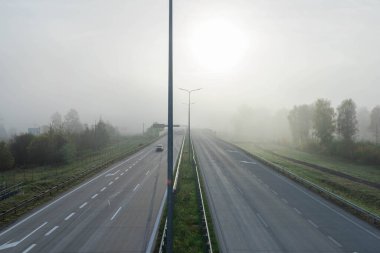 Çift şeritli otoyol, dört şeritli otoyol. Yol sisle kaplı, görüş mesafesini kısıtlıyor. Güneş tarafından önden aydınlatılır..