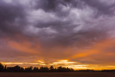 Koyu gri bulutlarla kaplı parlak bir gökyüzü. Batan güneşin kırmızı ışığı gökyüzünün açıkta kalan kısmına nüfuz eder ve resim çizgileri oluşturur..