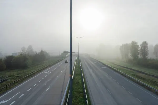 Çift şeritli otoyol, dört şeritli otoyol. Yol sisle kaplı, görüş mesafesini kısıtlıyor. Güneş tarafından önden aydınlatılır..
