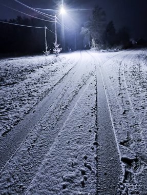 Kış gecesinde bir yol. Yüzey ve kenarlar bir kar tabakasıyla kaplıdır. Yol, araçların bıraktığı röleleri gösteriyor. Karanlık bir sokak lambasının ışığıyla aydınlanır..