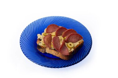 Bir dilim kızarmış ekmek, nohut humusu ve kızarmış salam dilimleri, mavi cam bir tabakta.