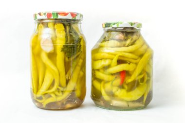 İki temiz cam kavanozda turşulu yeşil biber, beyaz arka planda izole edilmiş.