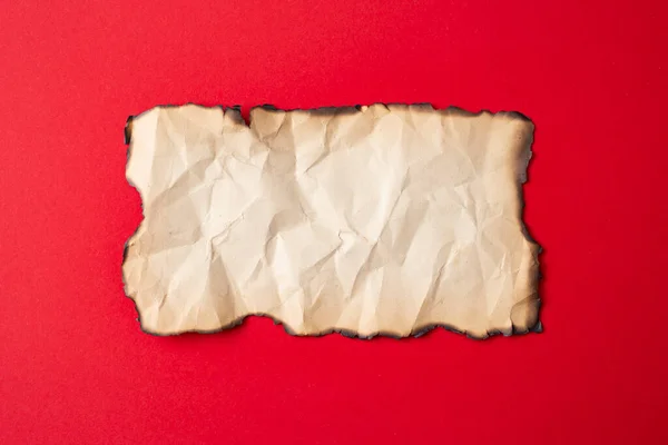 Vintage crumpled paper with burned edges, close up isolated on red background