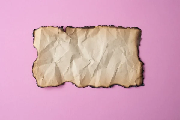 Vintage crumpled paper with burned edges, close up isolated on pink background